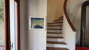 Un escalier avec des marches en bois et un radiateur rouge, un tableau encadré accroché au mur et une porte donnant sur l’extérieur.
