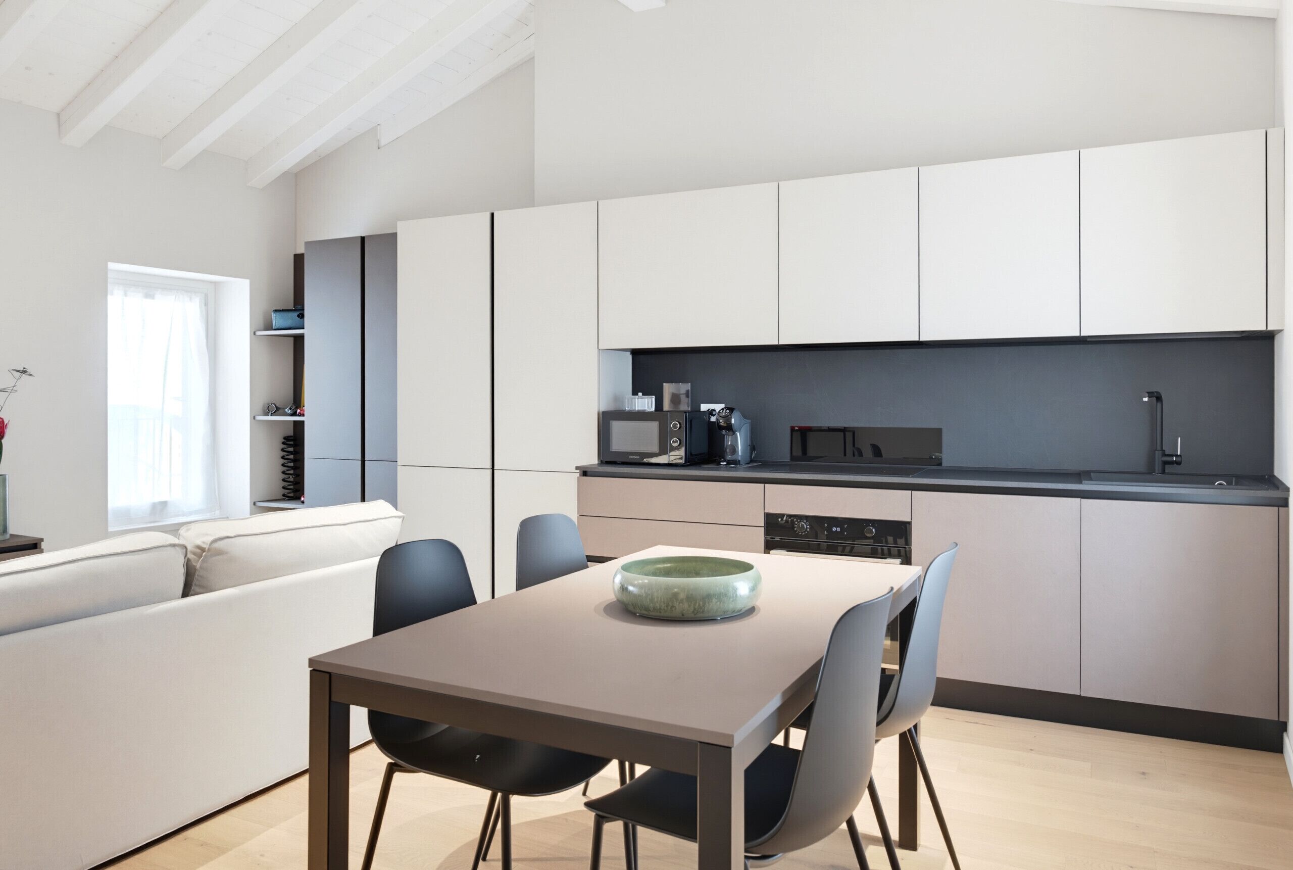 A modern kitchen with white cabinets, a dining table with chairs, and a built-in oven.