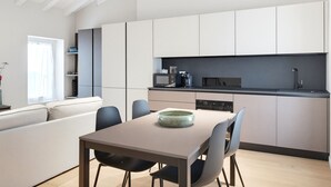 A modern kitchen with white cabinets, a dining table with chairs, and a built-in oven. - 1000 Miglia Apartment BSC (Brescia)