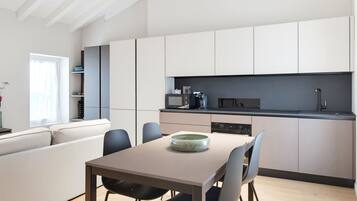 A modern kitchen with white cabinets, a dining table with chairs, and a built-in oven.