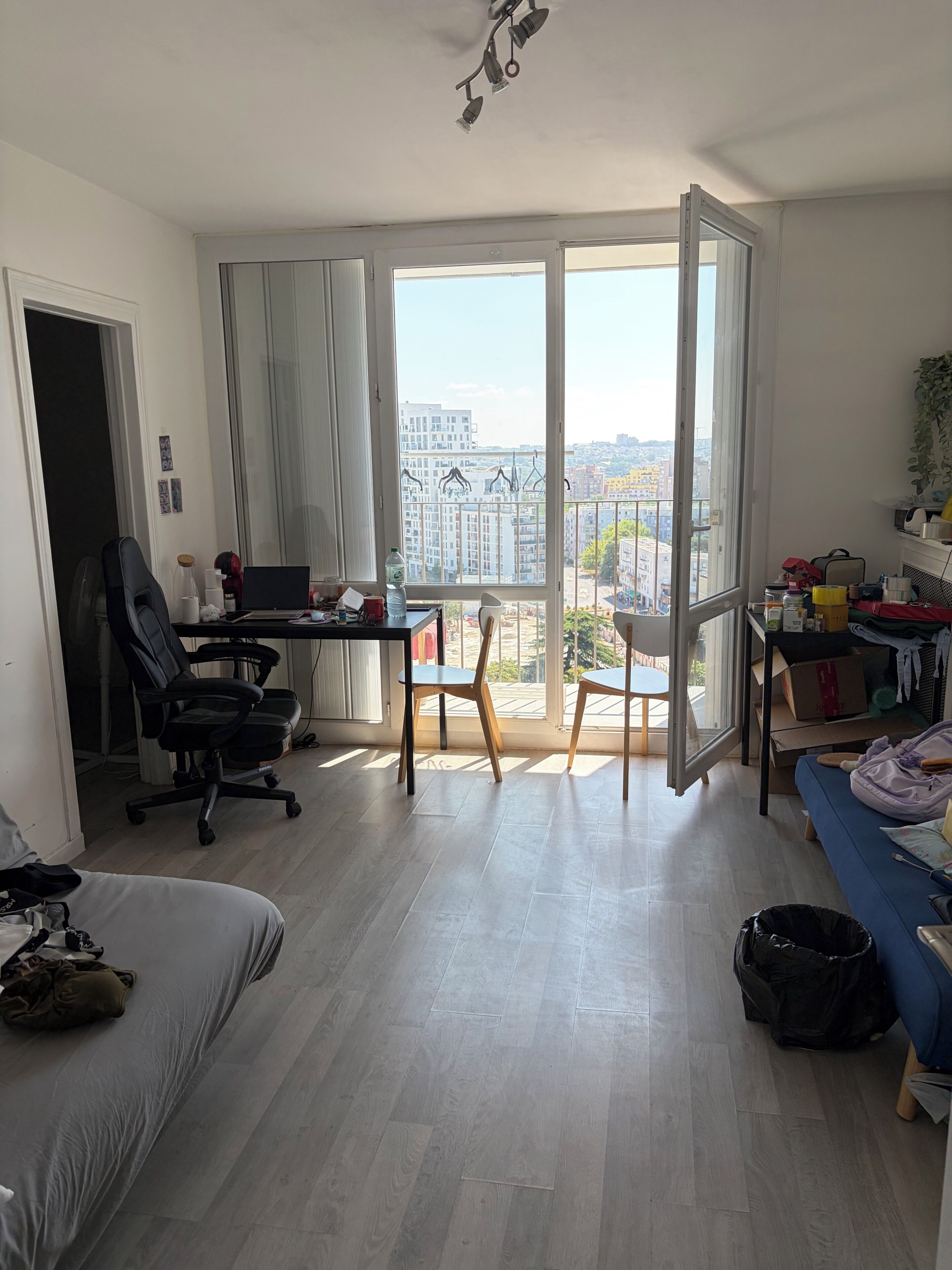 A modern apartment with a balcony, a desk with a laptop, a sofa, and a dining table.