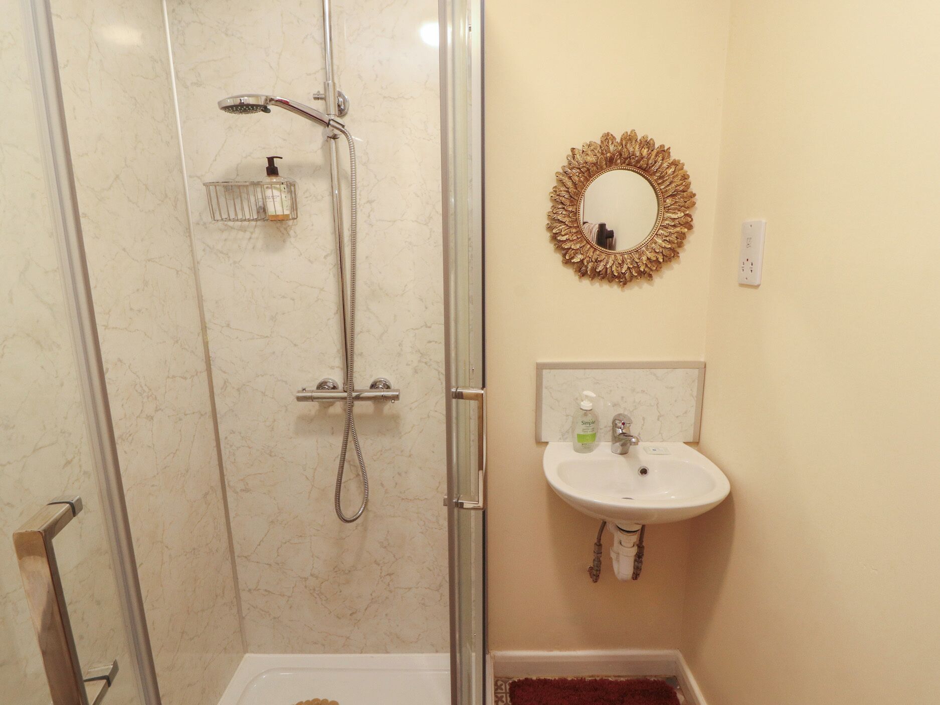 Une salle de bain dotée d’une douche à parois de verre, d’un lavabo blanc avec un plan-vasque en marbre et d’un miroir encadré d’or.