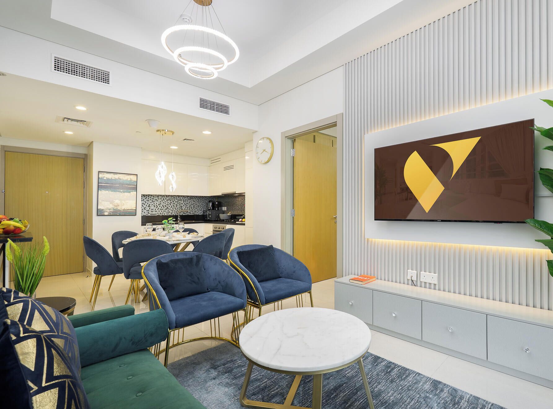 A modern hotel room with a dining area, a TV mounted on the wall, and a sofa.