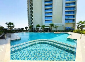 Una piscina con diseños de mosaicos, rodeada por un edificio de varios pisos y balcones.