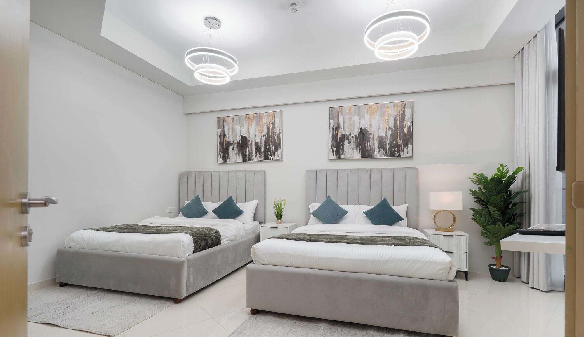 A modern bedroom with two beds, a nightstand, a lamp, and abstract wall art.