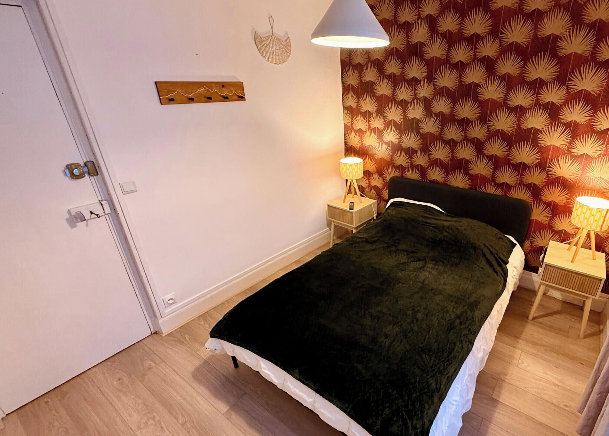 A bedroom with a bed, two bedside lamps, a door, and a wall with a leaf pattern.