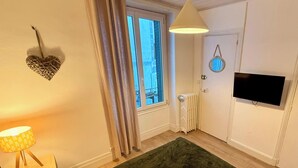 Ein Zimmer mit Bett, Vorhängen am Fenster, Heizkörper, Wand-Fernseher und Lampe.