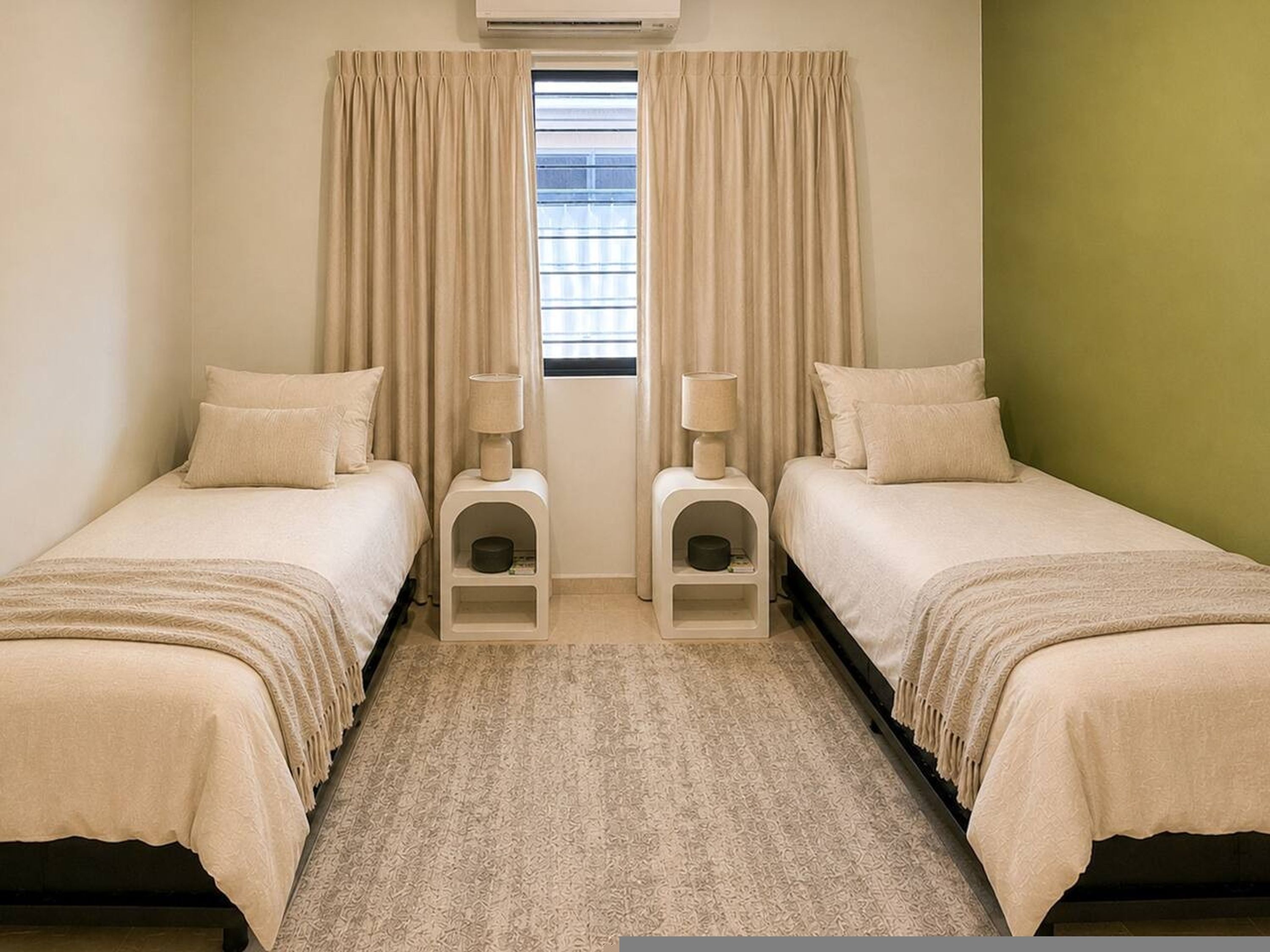 Habitación doble con dos camas, ventana con persianas, lámpara de pie y una pequeña estantería.