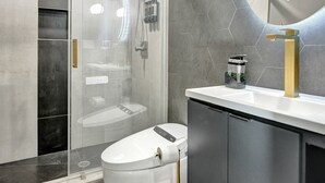 A modern bathroom with a glass-enclosed shower, a white toilet, a gold faucet, and a large mirror.