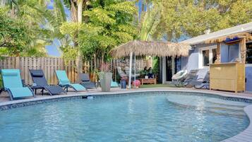 Une piscine avec des chaises longues, une clôture en bois et une végétation tropicale.