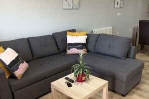 A grey sectional sofa with multiple cushions, a small wooden coffee table with a plant and remote controls, and a radiator in the background. - C19A02 Cozy Accommodations in Miengo (Miengo)
