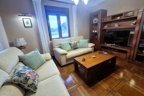 A living room with a sofa, a coffee table, a TV stand, and a window with curtains. - C19A02 Cozy Accommodations in Miengo (Miengo)
