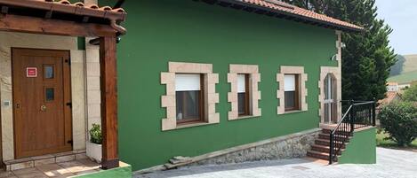 Ein Gebäude mit grüner Fassade, einer Holztür und einer Treppe, die zu einer oberen Ebene führt.