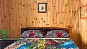A wooden-paneled room with a bed featuring a colorful landscape bedspread, a green nightstand, and a framed picture on the wall. - Dai Nonni Vacation Home | Between Gran Sasso and Rocca Calascio (Acciano)
