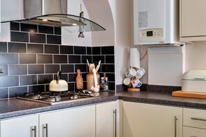 Une cuisine équipée d’une cuisinière à gaz, de carreaux noirs et blancs, d’une hotte en acier inoxydable et d’un four à micro-ondes placé au-dessus du plan de travail.
