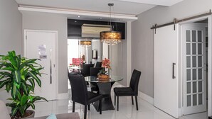 A modern dining area with a glass table, black chairs, a chandelier, and a potted plant. - Copacabana River (Rio de Janeiro)