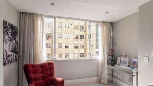 A room with a large window, a red chair, a reception desk, and a wall-mounted artwork. - Copacabana River (Rio de Janeiro)
