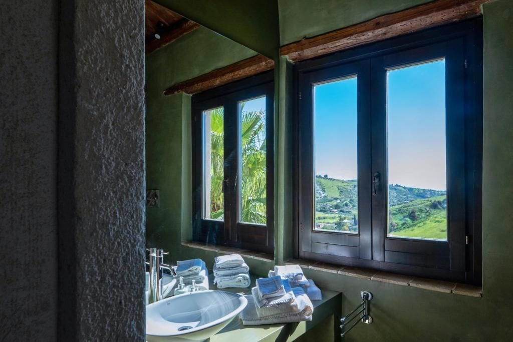 A bathroom with a sink, mirror, and window with a view of green hills.