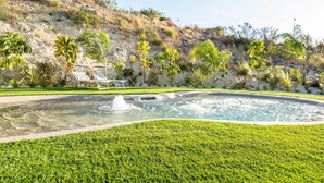 Ein Pool mit Wasserspiel, umgeben von gepflegtem Rasen und Palmen.