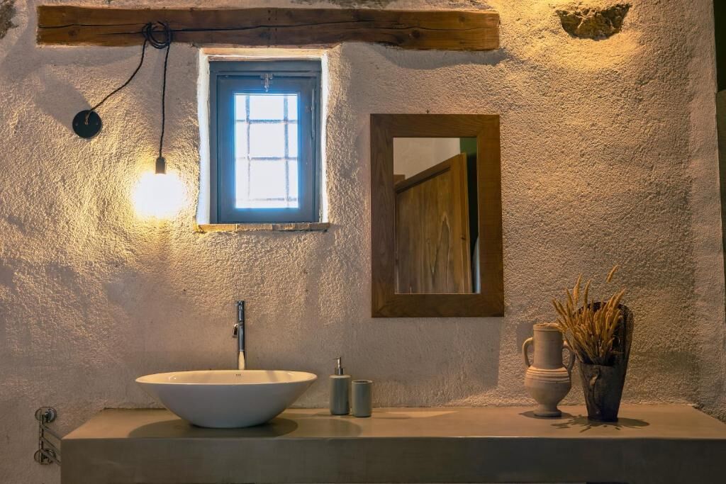 Une salle de bain avec un lavabo blanc, une petite fenêtre, un miroir et un luminaire.