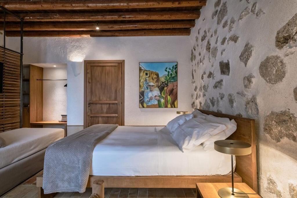 A bedroom with a wooden bed, a bedside table, a lamp, and a painting on the wall.