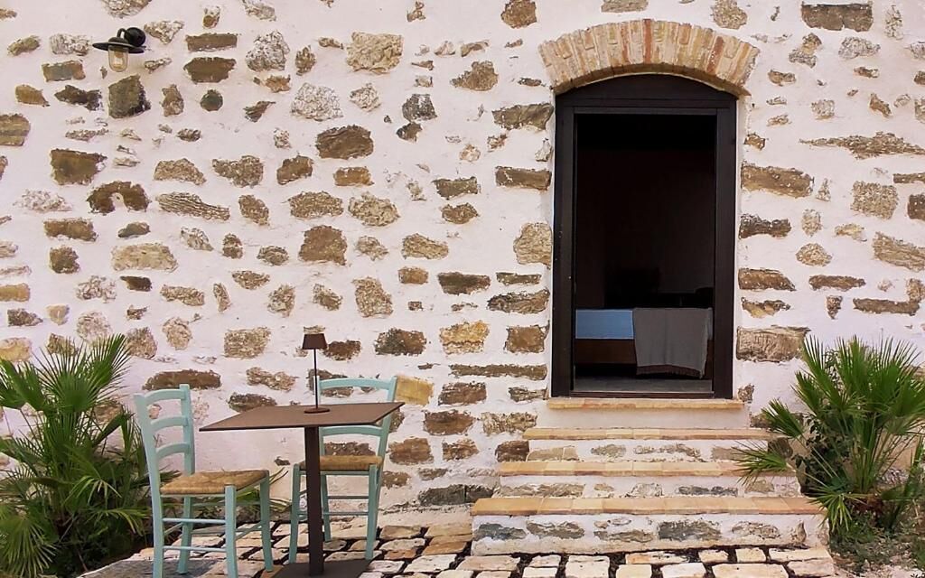 A stone building with a window and steps leading to an entrance. There is a table and two chairs outside.
