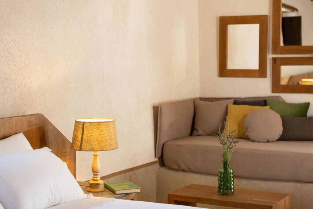 Una habitación de hotel con una cama, una mesita de noche con lámpara, un sofá con cojines y una pequeña mesa con un florero.