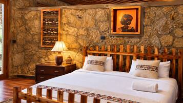 A bedroom with a stone wall, a wooden headboard, a bed with white linens, a nightstand with a lamp, and decorative pillows.