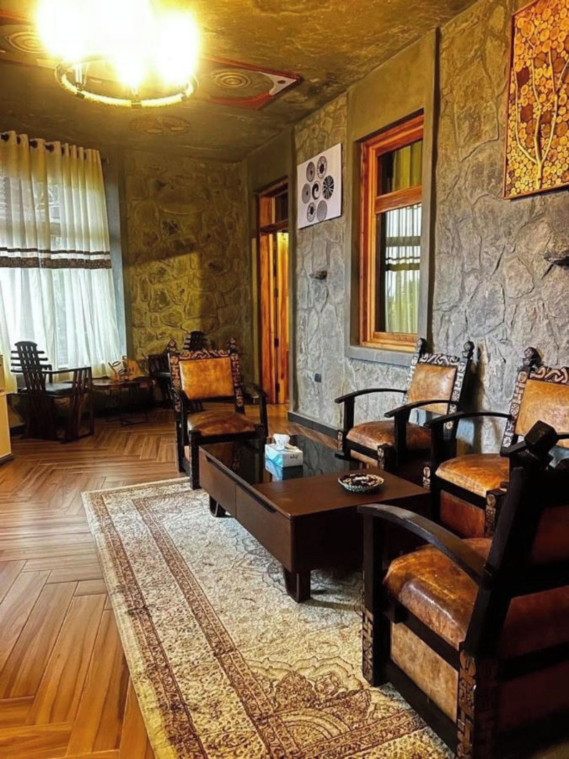 A room with a stone wall, wooden floor, and a fireplace. There are four wooden chairs and a coffee table.