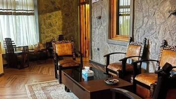 A room with a stone wall, wooden floor, and a fireplace. There are four wooden chairs and a coffee table.