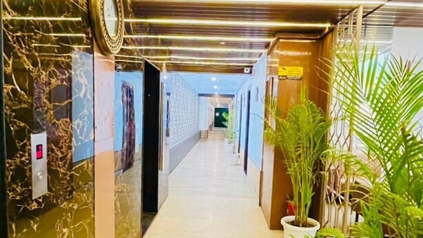 A hallway with a marble wall, a clock, and potted plants. - Hotel President Crown (Greater Noida)