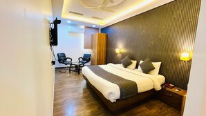 A hotel room with a bed, bedside table, wall-mounted TV, and a seating area with chairs. - Hotel President Crown (Greater Noida)