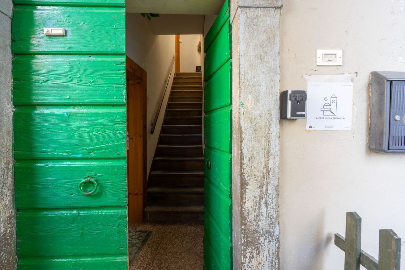 A staircase leading to a landing with a green door and a sign indicating a house on the terrace.
