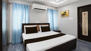 Habitación de hotel con cama, cortinas, aire acondicionado, un cuadro y una puerta con panel decorativo.