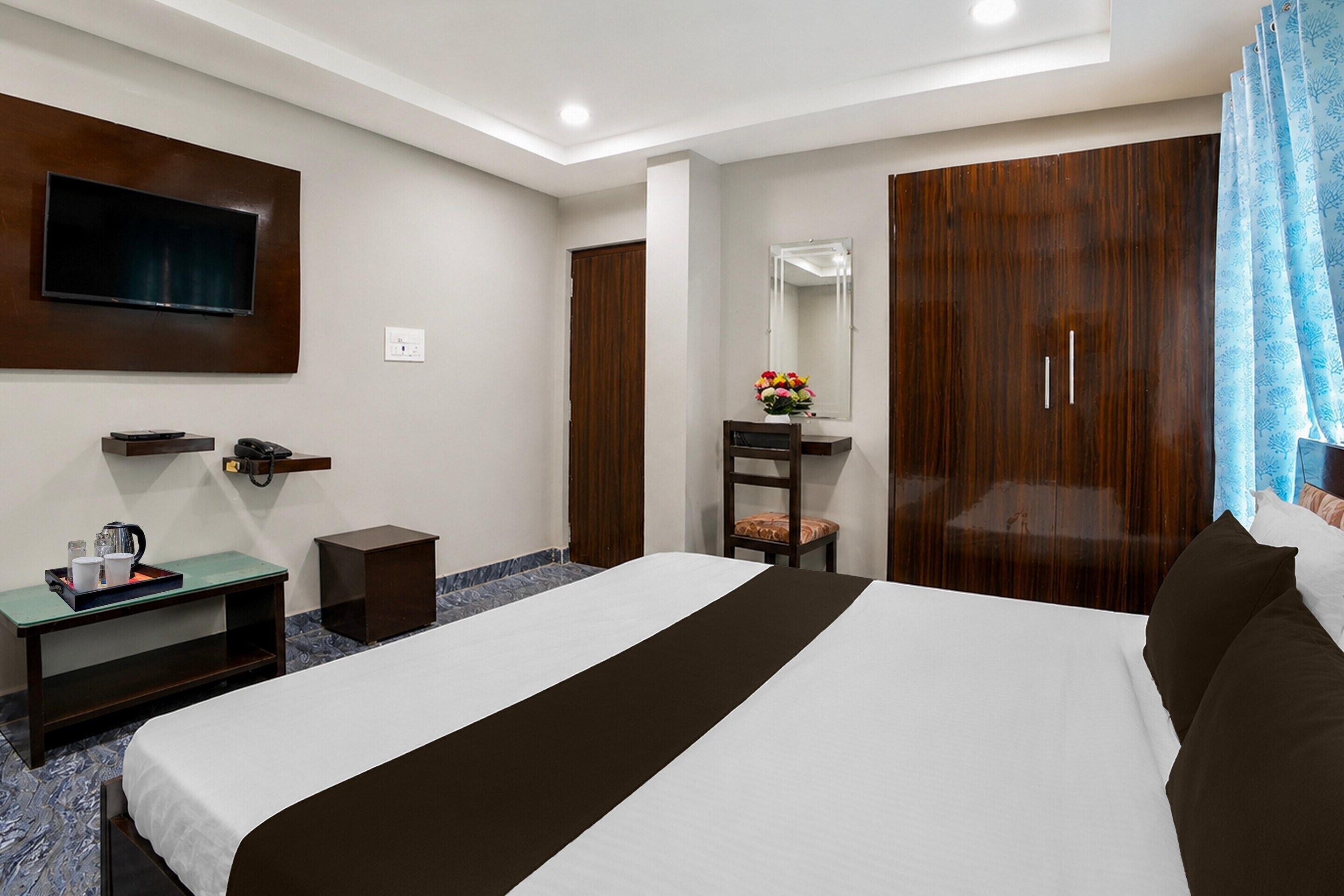 Habitación de hotel con cama, escritorio con teléfono, televisor de pantalla plana montado en la pared, espejo y armario.