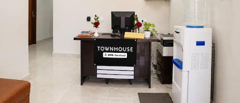 Mostrador de recepción con el rótulo 'TOWNHOUSE', un dispensador de agua, una computadora y una planta pequeña.