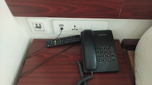 A wooden bedside table with a black Panasonic telephone and a remote control. - Raya Raj Anugraha (Kumbakonam)