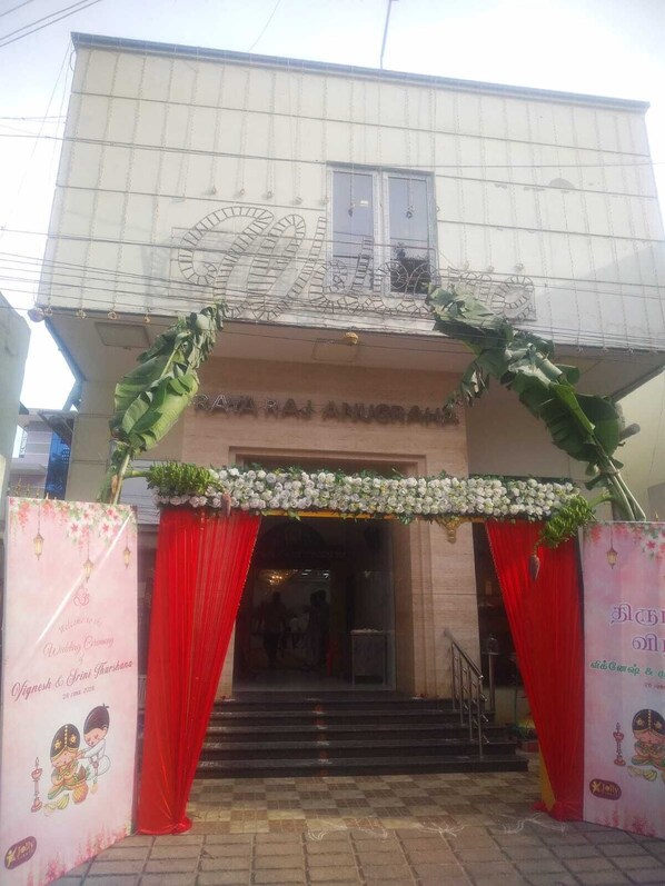 A building entrance with a red curtain, a floral arch, and a signboard.