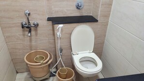 A bathroom with a toilet, two buckets, a shower, and a black shelf. - Raya Raj Anugraha (Kumbakonam)