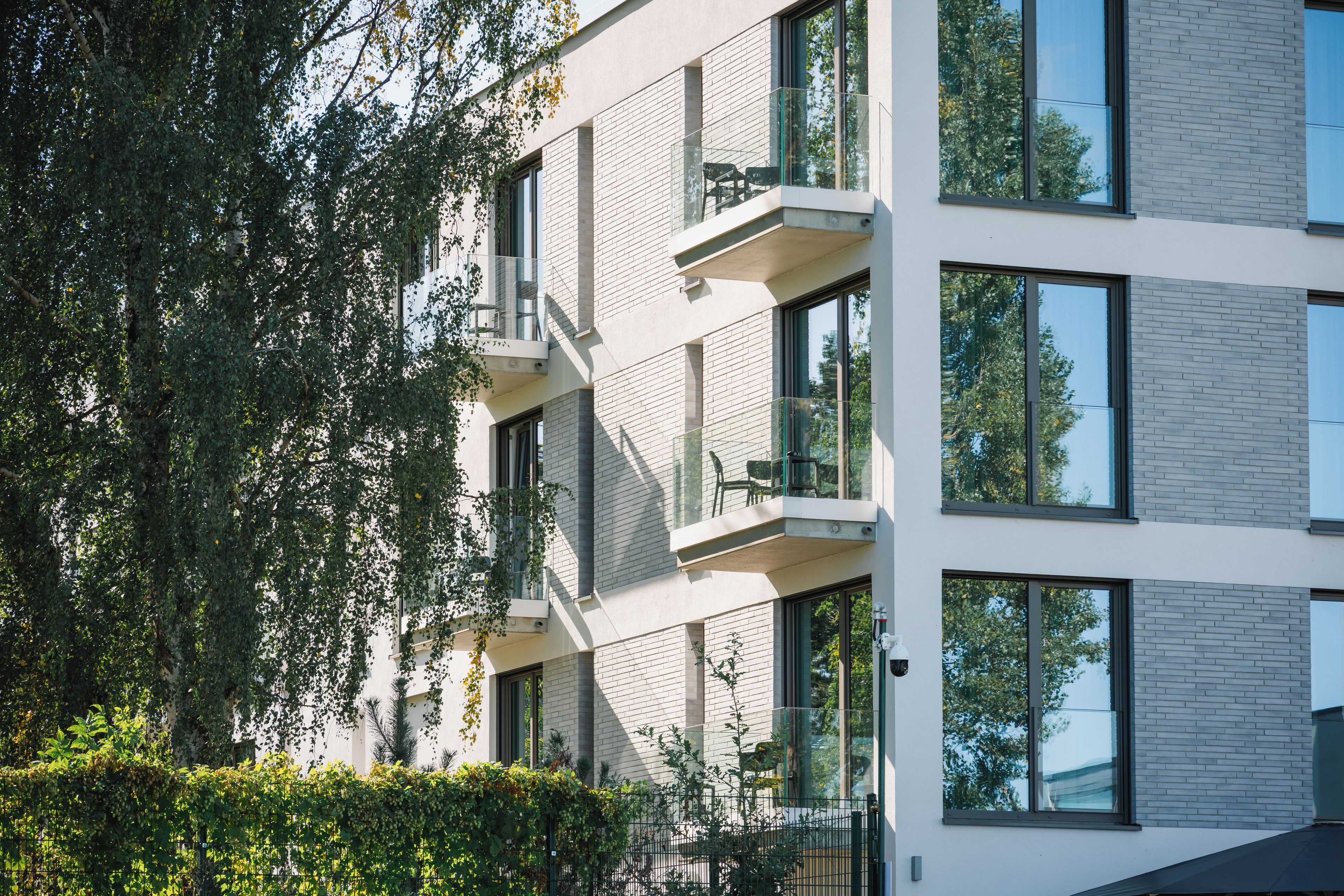 Ein mehrgeschossiges Gebäude mit moderner Architektur, das Balkone mit Glasgeländern und große Fenster aufweist.