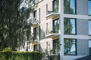 Un edificio de varios pisos con un diseño arquitectónico moderno, que presenta balcones con barandillas de vidrio y ventanas amplias.