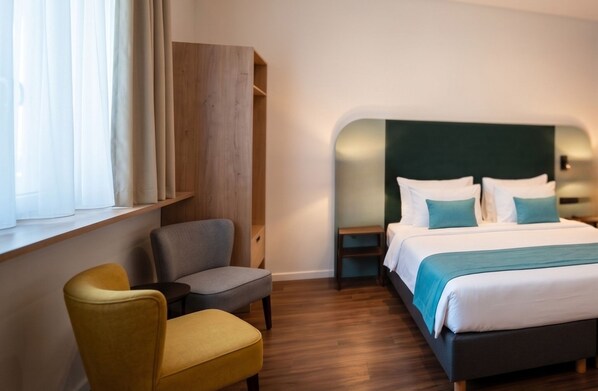 A hotel room with a bed, a chair, a small table, and a wardrobe. - H24 Hotel Berlin Grünau (Berlin)