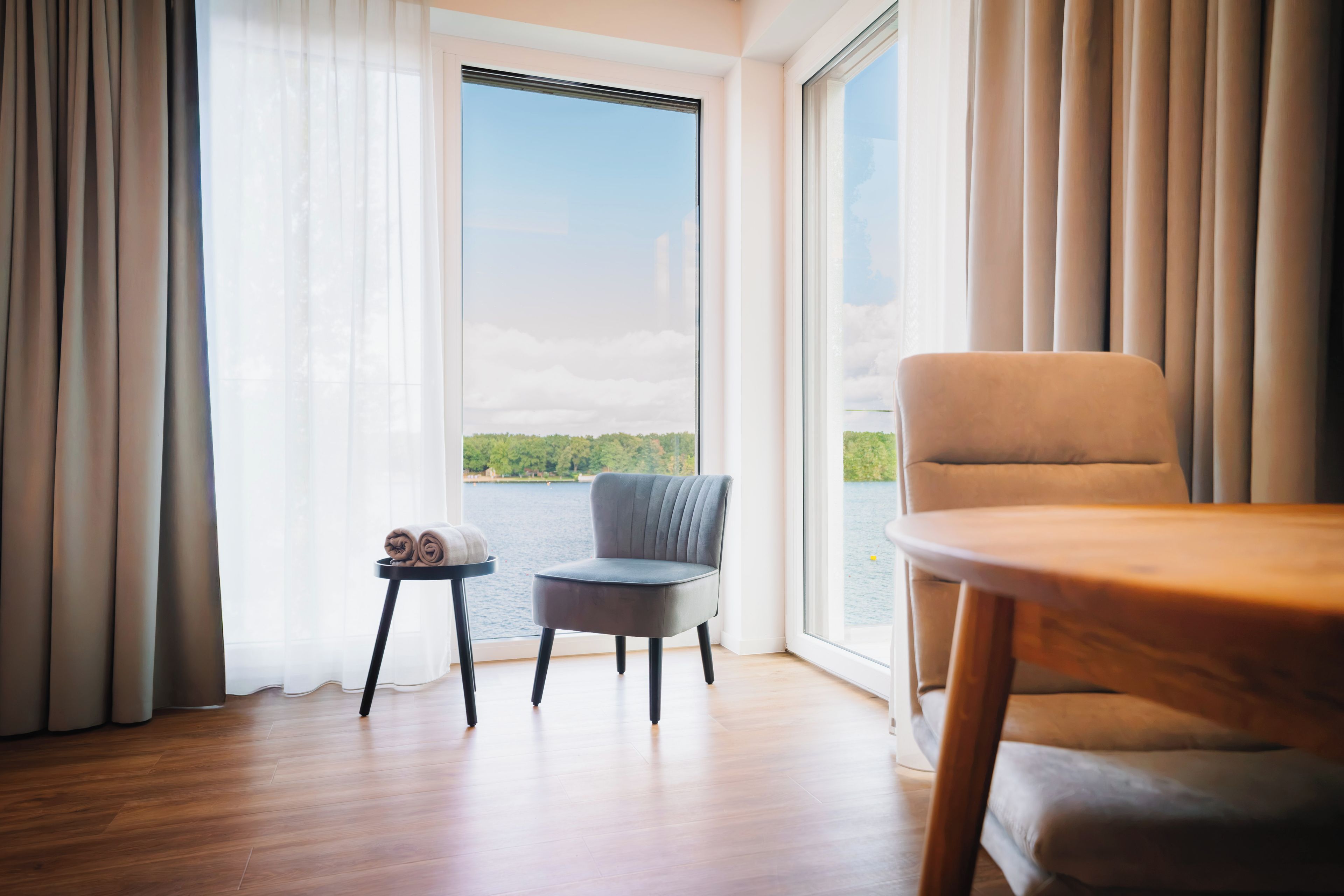 Una habitación con vistas a un lago, una silla, una mesita pequeña y una toalla enrollada sobre una mesita auxiliar.