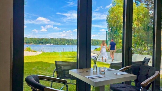 A dining area with a table and chairs, a view of a lake, and a grassy area with a pathway.
