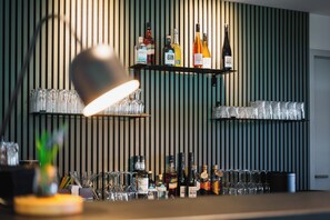 A bar area with shelves of liquor bottles and glasses, a hanging light fixture, and a striped wall. - H24 Hotel Berlin Grünau (Berlin)