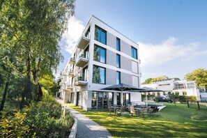 Un edificio residencial moderno de varios pisos con balcones, una zona de estar al aire libre cubierta y un césped bien cuidado.