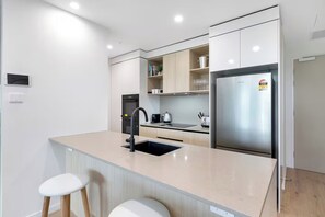 Eine moderne Küche mit einem Edelstahl-Kühlschrank, einem schwarzen Wasserhahn und einer beige gefärbten Arbeitsplatte.