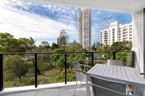 Un balcon avec une table et des chaises, donnant sur un paysage urbain avec de hauts immeubles et de la verdure.