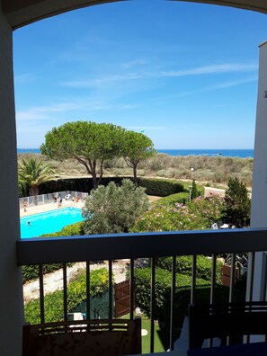 A view from a balcony overlooking a swimming pool, a large tree, and a distant body of water. - Near the beach, with an ocean view and a balcony (Saint-Cyprien)
