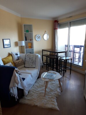A living room with a sofa, a small table, a bookshelf, and a dining area with chairs. - Near the beach, with an ocean view and a balcony (Saint-Cyprien)
